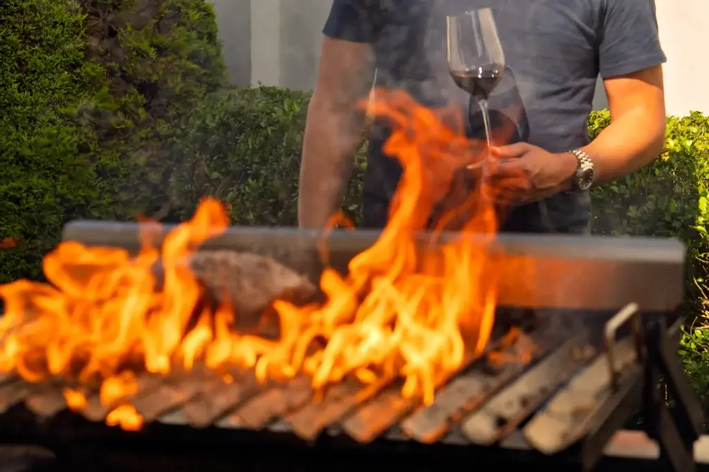 Copa de vino tinto junto a las brasas y cortes de carne en un asado chileno
